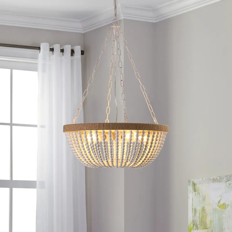 The Willow Beaded Chandelier suspended in a bright neutral-toned room near a large window, featuring a round natural wood-finished frame, layered white wooden bead strands forming a curved basket silhouette, exposed warm-glowing bulbs, and a chain-hung ceiling mount.