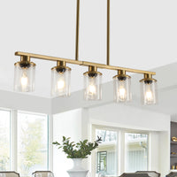 Brass Ashcombe Glass Shade Chandelier hanging in a bright kitchen, featuring five illuminated clear glass cylinder shades arranged along a horizontal brass bar.