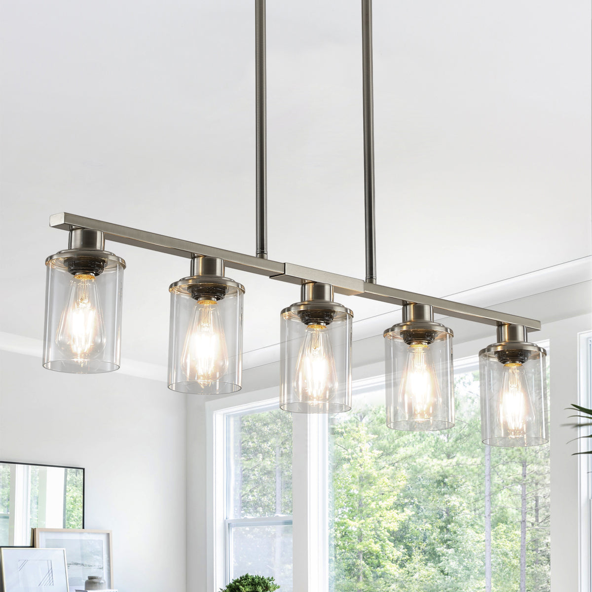 Close-up view of the Ashcombe Glass Shade Chandelier in a brushed metal finish, featuring a horizontal five-light bar, clear cylindrical glass shades, and adjustable hanging rods.